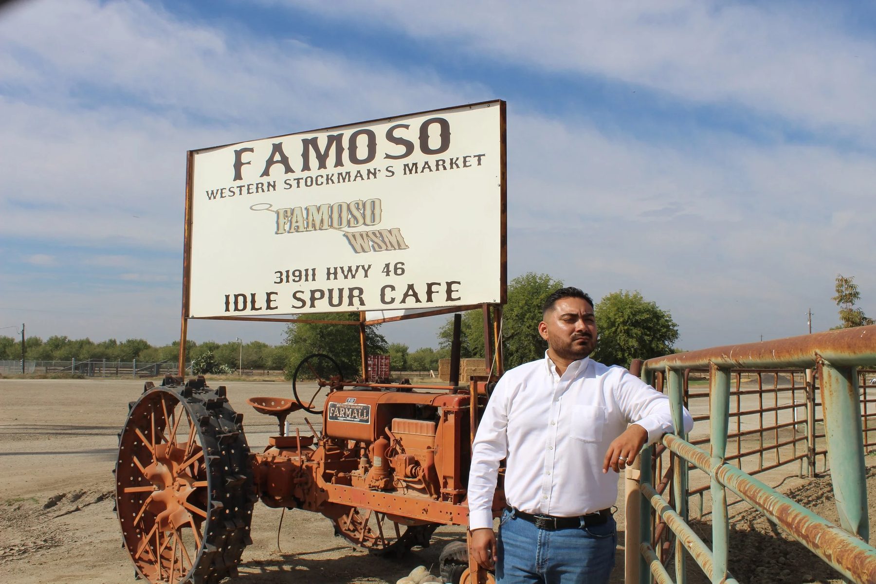 Guillermo beside an old tractor at the Famoso stockyard sign.
